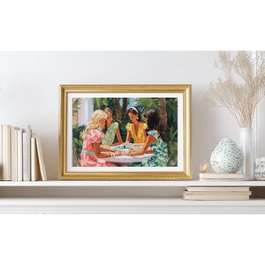 May include: A framed print depicts four women playing a game at a round table. The women are dressed in colorful dresses, with a lush green background of palm trees. The frame is gold.