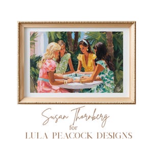 May include: A framed art print featuring a painting of four women playing a game outdoors. The women are dressed in colorful dresses, and the artwork is set in a gold frame. The artist's name and design studio are displayed below the artwork.
