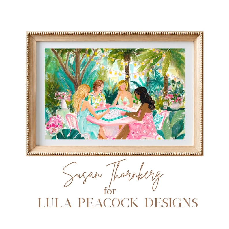K&ouml;nnte beinhalten: Ein gerahmter Kunstdruck mit einem Gem&auml;lde von vier Personen, die an einem rosa Tisch in einem &uuml;ppigen Garten mit Lichterketten ein Brettspiel spielen. Der Text darunter lautet Susan Thornberg for LULA PEACOCK DESIGNS in brauner Schrift.