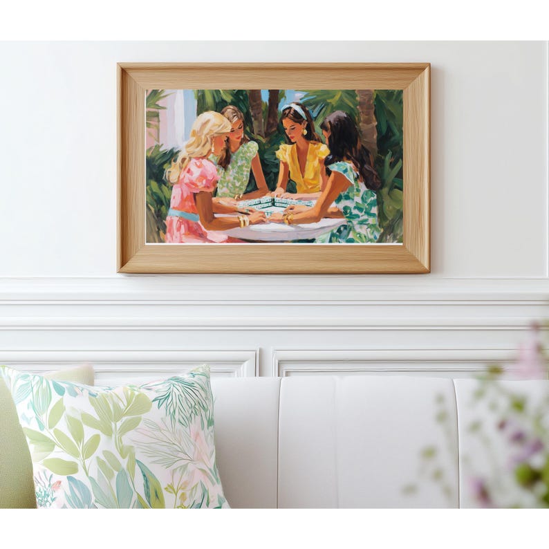 May include: A framed print depicts four women gathered around a table, engaged in a game. The artwork features a light wood frame and a vibrant color palette, with the women wearing dresses in shades of pink, green, and yellow. The background includes lush greenery.
