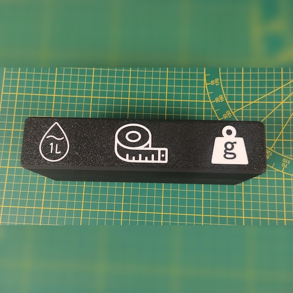 Closed black storage case shown close-up on a green work surface with white volume, length, and mass icons.