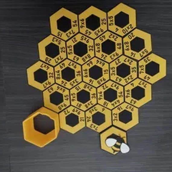 Complete yellow-and-black HoneyHex multiplication puzzle with its storage box and bee lid beside it on a dark wood table.