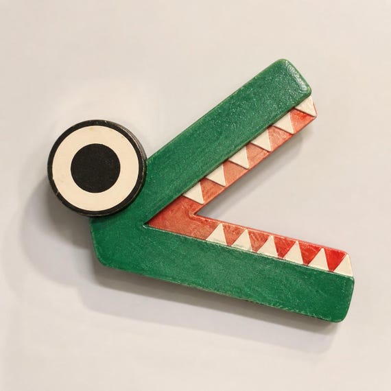 Green less-than ChompCompare crocodile with coral-red mouth, white teeth, and one large eye on a blank whiteboard.