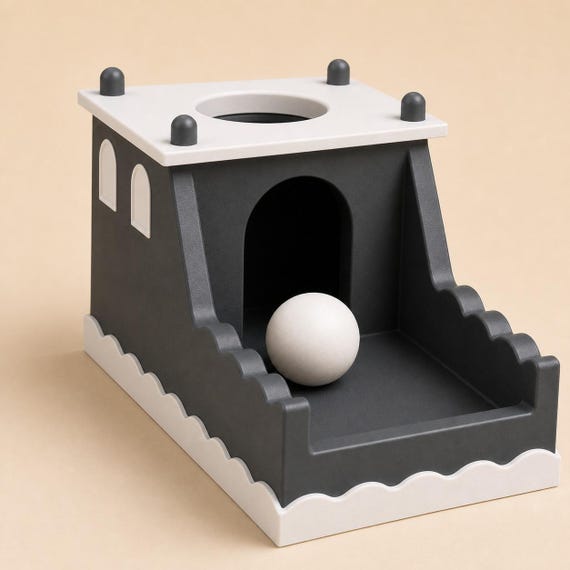 Close low-angle view of one ivory ball emerging through the front arch of the charcoal CastlePeek toy.