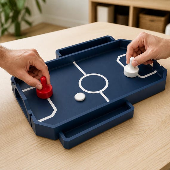 Two adult hands playing the fully assembled Dark Blue RinkRush table hockey game with red and white pushers on a light wood table