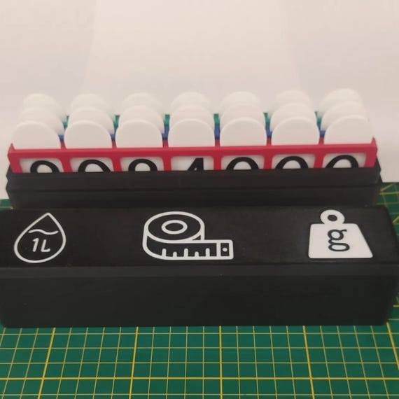 Open black storage case holding the three colored metric boards, with white volume, length, and mass icons visible on the lid.