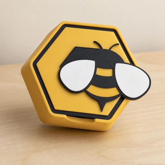 Closed yellow hexagonal HoneyHex storage box with a raised black-and-yellow bee and white wings on a pale wood table.