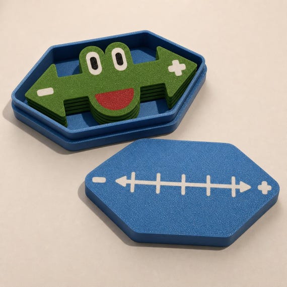 Open blue storage tray holding four stacked green frog markers with the decorated lid resting beside it.