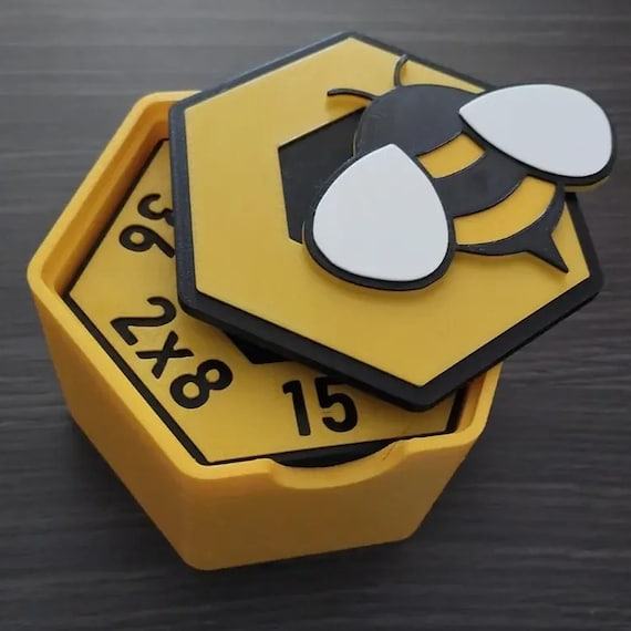 Yellow HoneyHex storage box viewed close-up with multiplication tiles inside and the bee-decorated lid angled over the opening.
