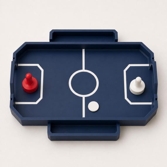 Near-overhead view of the Dark Blue RinkRush table hockey game with two attached catch trays, two pushers, and one Ivory White puck