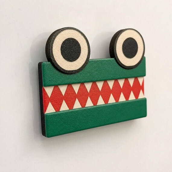 Green equal-sign ChompCompare crocodile with two eyes and opposing white teeth viewed close-up on a blank whiteboard.