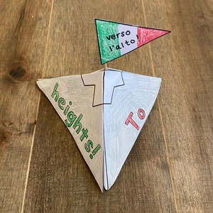 May include: A paper pyramid with the words "To heights!" on one side and a flag with the words "verso l'alto!" on top.