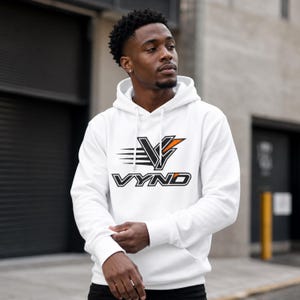 May include: A white hooded sweatshirt featuring a graphic logo on the chest. The logo displays the text VYNO in a bold, black, and orange outlined font, positioned below a stylized V symbol with horizontal motion lines and an orange accent.