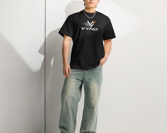 May include: A black short-sleeved t-shirt featuring a white and orange graphic logo on the chest that reads VYND with a stylized V symbol above the text. The shirt has a crew neckline and is worn with light blue denim jeans and sneakers.