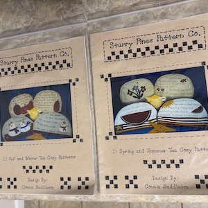 May include: Two Starry Pines Pattern Co. craft pattern booklets in clear plastic sleeves. One booklet features 21 Fall and Winter Tea Cozy Patterns, and the other features 21 Spring and Summer Tea Cozy Patterns, both designed by Connie Huddleson.