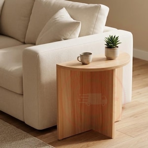 May include: A semi-circular side table made of light-toned wood with a vertical support base. A small, plain ceramic mug and a potted succulent plant in a light-coloured pot are placed on the flat surface of the table.