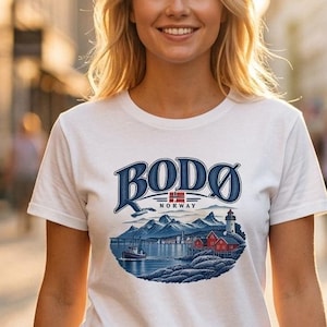 May include: A white short-sleeved t-shirt featuring a graphic print of a coastal landscape with mountains, a lighthouse, and red buildings. The text "BODØ NORWAY" is printed in blue above the illustration, which includes a small Norwegian flag.