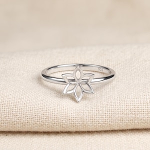 Peut inclure: Une bague en argent poli présentant un motif floral ajouré à six pétales au centre. L'intérieur de l'anneau porte clairement l'inscription 925, indiquant la composition métallique de ce bijou délicat et finement travaillé.