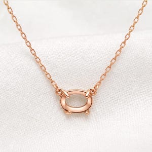 May include: A rose gold necklace featuring a delicate chain and a central horizontal oval pendant. The pendant is smooth and polished, connected to the chain by two small loops on each side, creating a clean and simple design for this piece of jewelry.