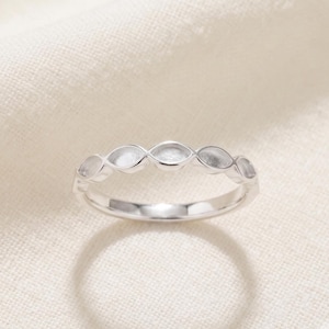Könnte beinhalten: Ein silberfarbener Ring, der aus einer Reihe miteinander verbundener marquiseförmiger Elemente besteht, die ein durchgehendes Band bilden. Das Metall hat eine glatte, polierte Oberfläche mit reflektierendem Glanz und einem sich wiederholenden Muster.