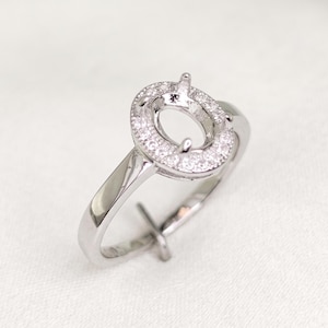 Peut inclure: Une monture de bague argentée dotée d'une tête ovale en halo conçue pour accueillir une pierre centrale. Le halo est incrusté de petites pierres claires et scintillantes, et l'anneau est lisse et poli, présentant une structure métallique raffinée.