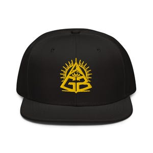 May include: A black snapback cap featuring a yellow embroidered design on the front. The embroidery depicts a pyramid with an eye at the top, surrounded by radiating sun rays, with the letters GB positioned prominently at the base of the pyramid.