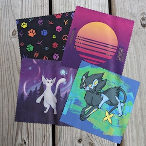 May include: Four different microfiber cleaning cloths with colorful designs. One cloth features a black background with paw prints and bird silhouettes. Another cloth has a purple background with a white cat-like creature. A third cloth has a blue background with a black and blue creature with yellow eyes. The final cloth has a purple background with a sunset and city skyline.