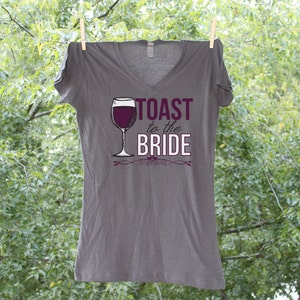 May include: Gray V-neck t-shirt with a graphic of a wine glass and the text "TOAST to the BRIDE".
