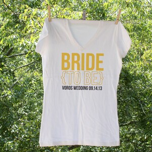 May include: White t-shirt with the text "Bride {to be}" in yellow and "Voros Wedding 09.14.13" in black.