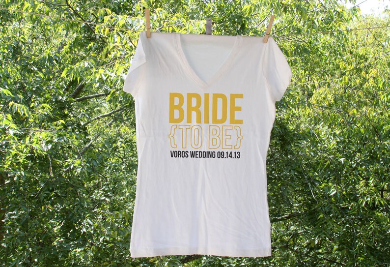 May include: White t-shirt with the text "Bride {to be}" in yellow and "Voros Wedding 09.14.13" in black.