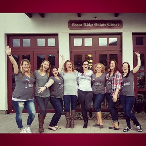 May include: A group of eight women wearing shirts with the word "Bride" on them, posing in front of a building with the sign "Goose Ridge Estate Winery".