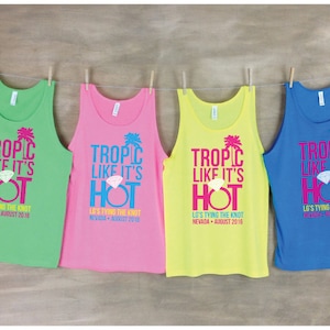 May include: Four tank tops with the text "Tropic Like It's Hot" printed on them. The tank tops are in green, pink, yellow, and blue. Each tank top has a diamond ring and palm tree graphic. The text "Lo's Tying the Knot" is printed below the main text.