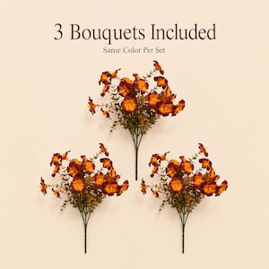 May include: Three artificial flower bouquets featuring deep burgundy and vibrant orange petals with green stems and foliage. The text 3 Bouquets Included and Same Color Per Set is displayed above the floral arrangements on a light background.