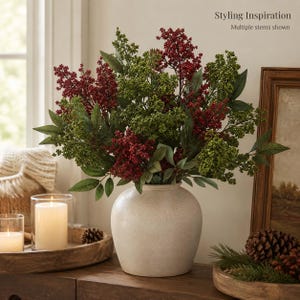 Può includere: Un vaso in ceramica beige opaco di forma rotonda contiene una grande composizione di rami di bacche artificiali rosso scuro e verdi. I rami presentano grappoli di piccole bacche e foglie appuntite. In alto a destra appare il testo Styling Inspiration.