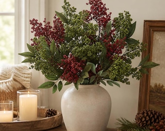 May include: A round, matte beige ceramic vase holds a large arrangement of artificial berry stems in deep red and green. The stems feature clusters of small berries and pointed leaves. Text in the upper right corner reads Styling Inspiration.