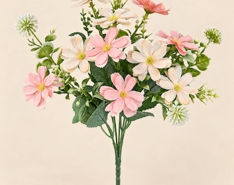 May include: A bouquet of artificial flowers featuring pink and cream-colored petals with yellow centers. The arrangement includes green leaves and small, round, white textured floral accents on thin stems, all gathered into a single base.