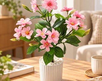 May include: A potted artificial plant featuring vibrant pink flowers with yellow centers and deep green leaves. The plant is housed in a white, vertically ribbed cylindrical ceramic pot filled with small white decorative stones.
