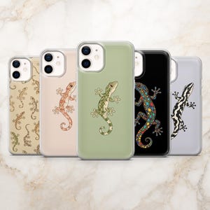 May include: Five smartphone cases arranged in a row, each featuring a unique gecko design. The designs include a beige case with a repeating gecko pattern, a peach case, a sage green case, a black case with a colourful dotted gecko, and a light grey case.