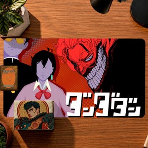 Peut inclure: Un tapis de jeu rectangulaire illustré de personnages de style anime, dont une figure au large sourire édenté et aux cheveux rouges, ainsi qu'une personne aux cheveux noirs avec un nœud papillon rouge. Le texte "ダンダダン" est en blanc.
