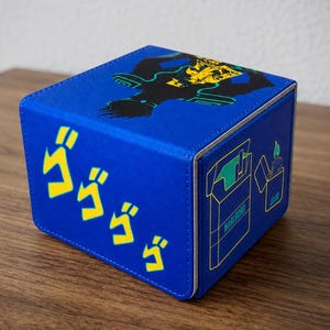 Könnte beinhalten: Eine blaue, rechteckige Aufbewahrungsbox mit einer gelben Grafik einer Figur auf der Oberseite, gelben japanischen Katakana-Schriftzeichen auf der Vorderseite und einer grünen Umrisszeichnung einer Zigarettenschachtel und eines Feuerzeugs.