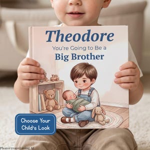 Peut inclure: Un livre relié intitulé Theodore You're Going to Be a Big Brother, illustré d'un enfant tenant un nouveau-né, un ours en peluche et un lapin en jouet sur un tapis, avec un petit encadré bleu indiquant Choose Your Child's Look.