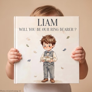 May include: A square book with a cream-colored cover featuring the text LIAM WILL YOU BE OUR RING BEARER? and an illustration of a young boy in a grey vest, trousers, and bow tie holding a ring pillow with two gold rings on it.