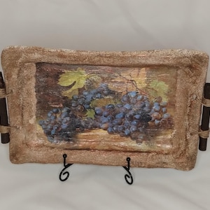May include: A rectangular serving tray with a textured, stone-like border and a central image of dark purple grapes on a vine. The tray features two dark brown cylindrical handles on the sides, each secured with light-coloured twine wrapping.