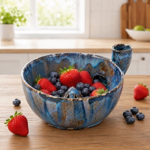 May include: A round, blue and brown glazed ceramic citrus juicer bowl filled with fresh strawberries and blueberries. The bowl features a central reamer for juicing and a side handle for pouring, with a textured, drip-style glaze finish.
