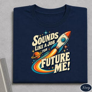 Puede incluir: Una camiseta azul marino con un gráfico de un cohete despegando al espacio junto a un planeta y estrellas. El texto "SOUNDS LIKE A JOB FOR FUTURE ME!" aparece en una fuente retro llamativa con detalles en naranja, amarillo y azul claro.