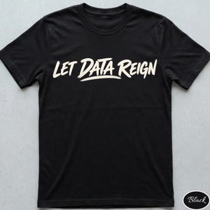 Pode incluir: Uma t-shirt preta de manga curta com o texto "LET DATA REIGN" impresso num tom branco sujo com uma tipografia ousada estilo pincel no peito. A peça possui gola redonda e um corte padrão, apresentando um design simples e limpo.