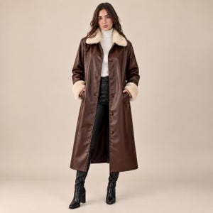 May include: A long, dark brown coat featuring a cream-colored faux fur collar and matching faux fur cuffs. The coat has a button-front closure and is worn over a white turtleneck sweater and black trousers, paired with black heeled boots.