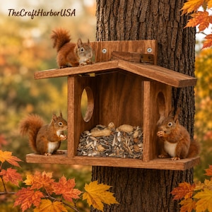 May include: A brown wooden squirrel feeder mounted on a tree trunk, featuring a gabled roof, circular side openings, and a central compartment filled with mixed nuts and seeds. Three red squirrels are positioned on the structure.