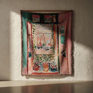 Pode incluir: Uma tapeçaria de parede tecida apresentando uma cena de estilo impressionista de uma janela aberta com vista para uma costa com veleiros, plantas em vasos e tons vibrantes de verde, rosa, azul e vermelho com uma borda de franjas.