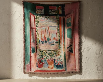 May include: A woven tapestry wall hanging featuring a colourful impressionist-style scene of an open window overlooking a coastal view with sailboats, potted plants, and vibrant shades of green, pink, blue, and red with a fringed edge.